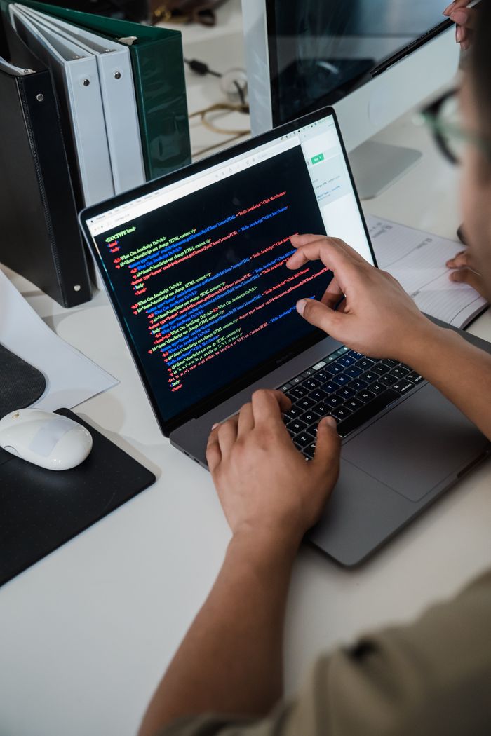 services-img Close-up of a programmer pointing at a colorful code script on a laptop in an office setting.