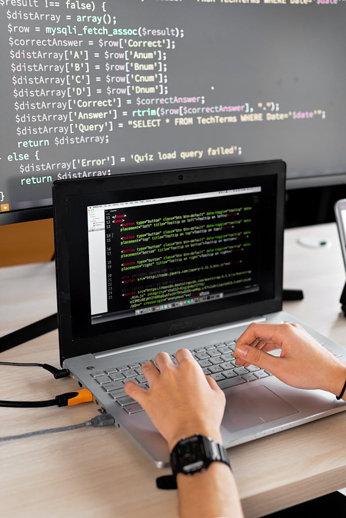 services-03 Person coding at a desk with laptop and external monitor showing programming code.